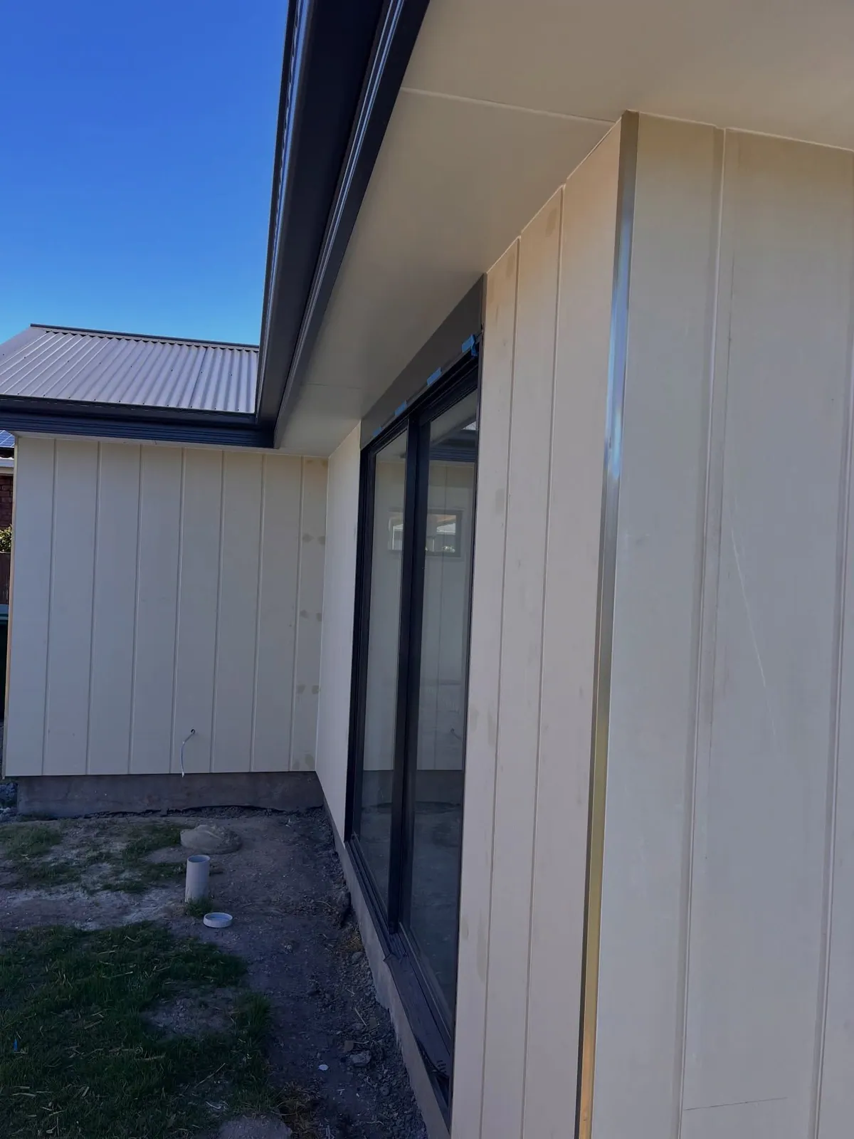 Pale vertical cladding and a dark-framed sliding door along the side of a new build
