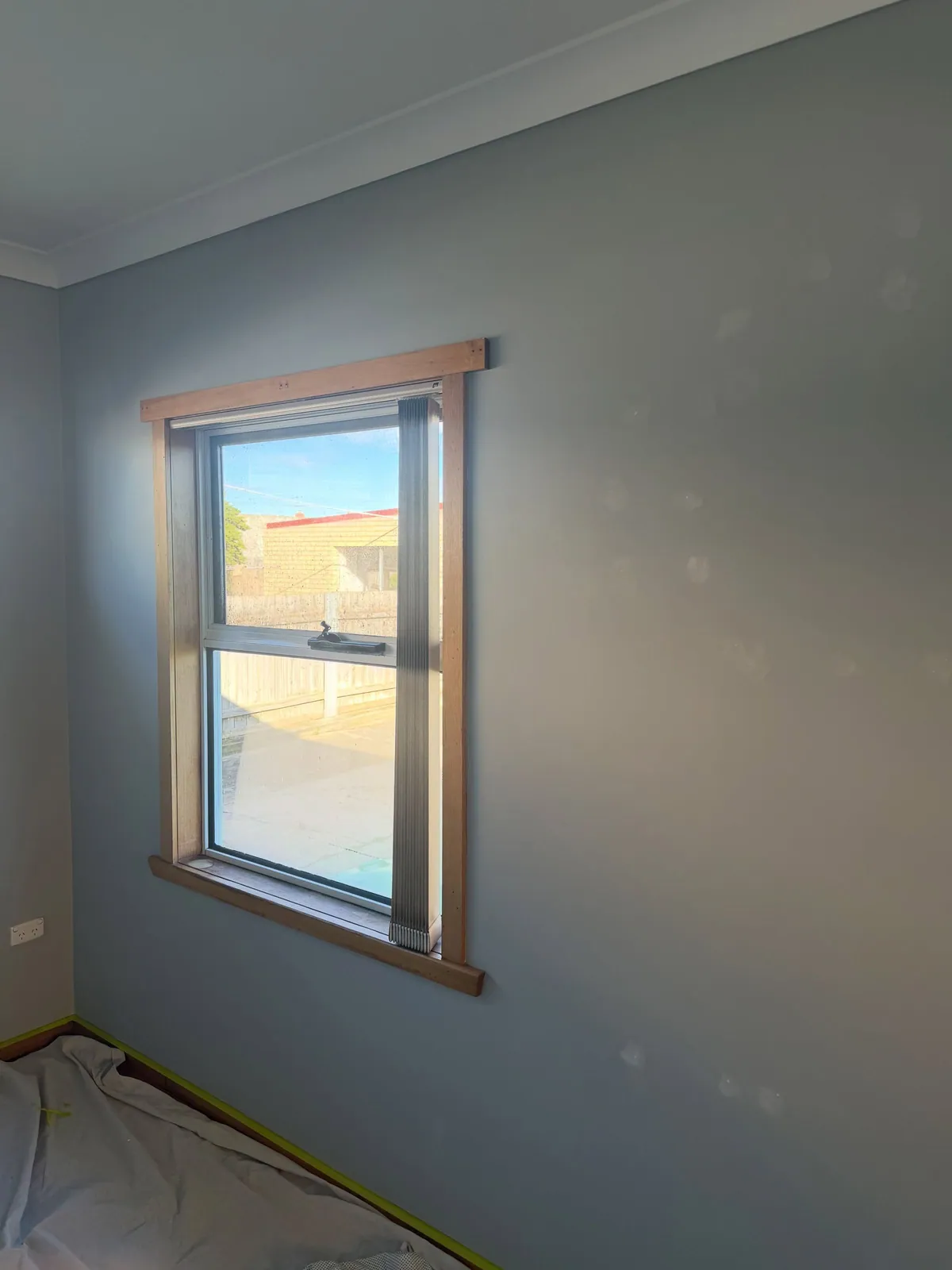 Bedroom wall in a dark grey-blue around a timber-framed window, before a repaint